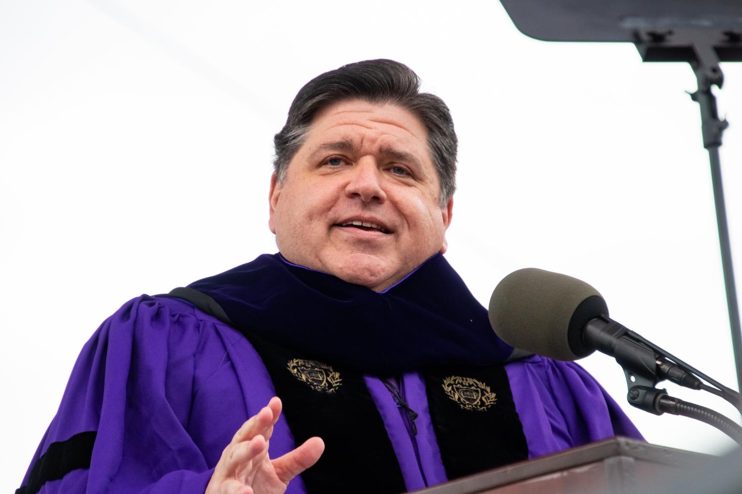 A person in a purple robe and black stole talks into a microphone at a podium.
