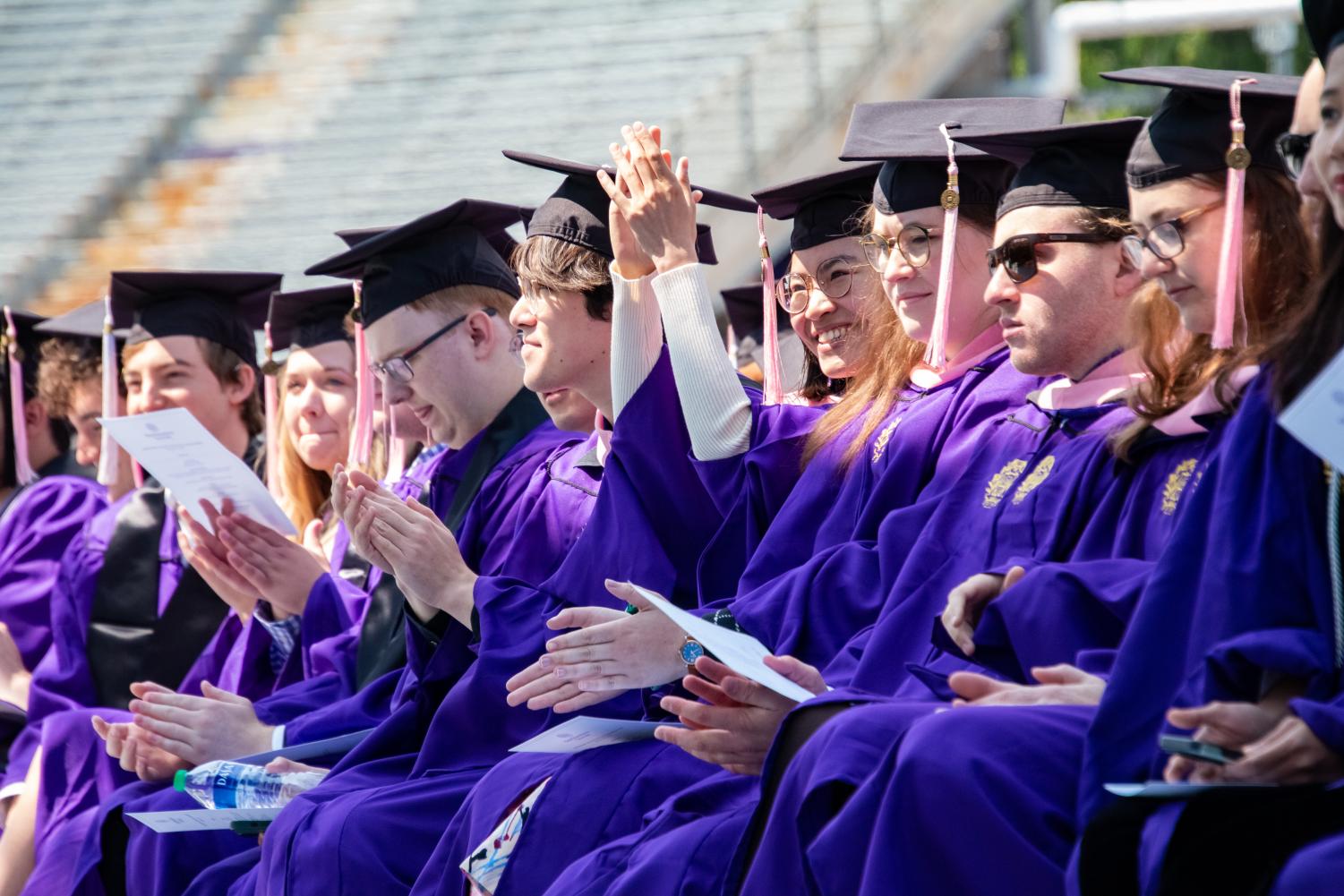 Students in purple robes clap.