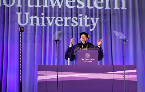 A man in a purple robe speaks at a podium with his arms up.