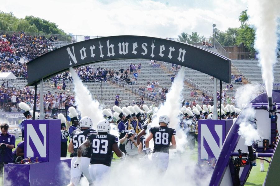 Players in purple jerseys and white helmets walk under a gray arch that says ‘Northwestern.’
