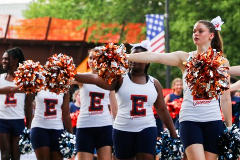 Cheerleaders point orange and silver pom poms. 