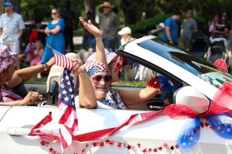 A woman waves an American flag from a car decorated in red, white and blue.
