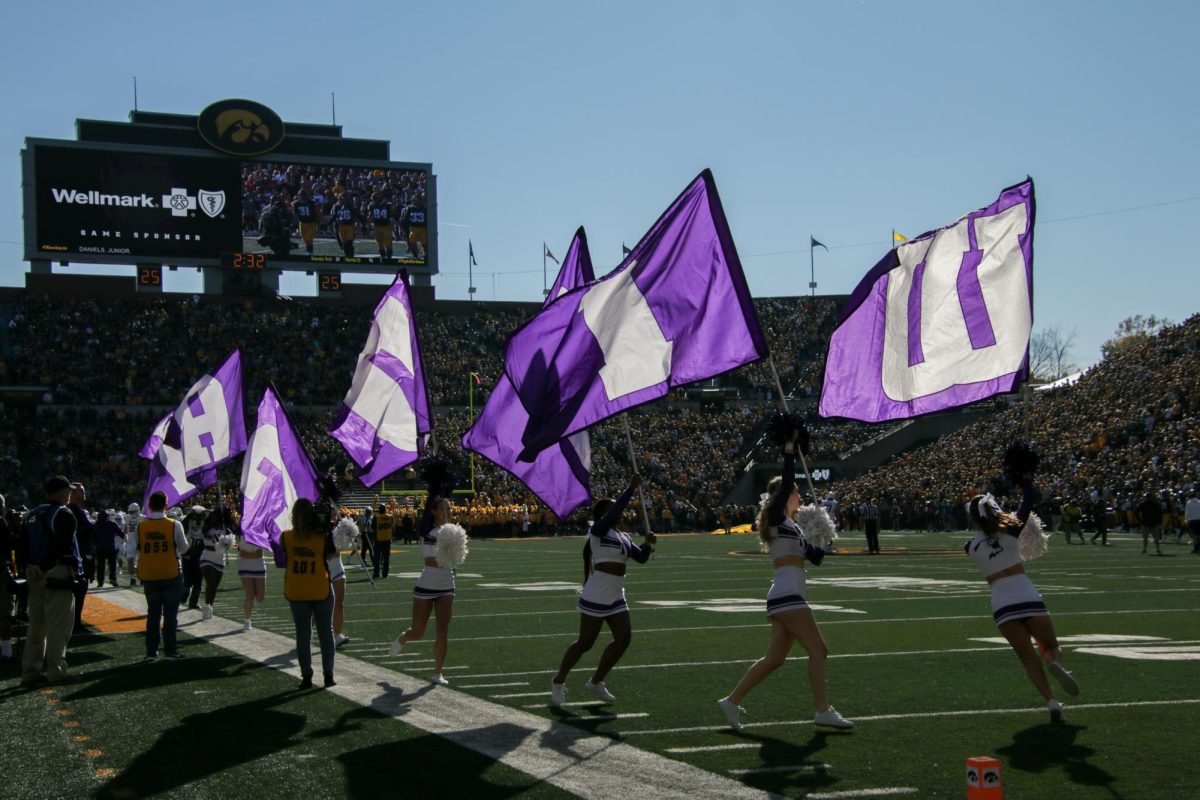 Northwestern cheerleaders wave NU flag before contest against Iowa.