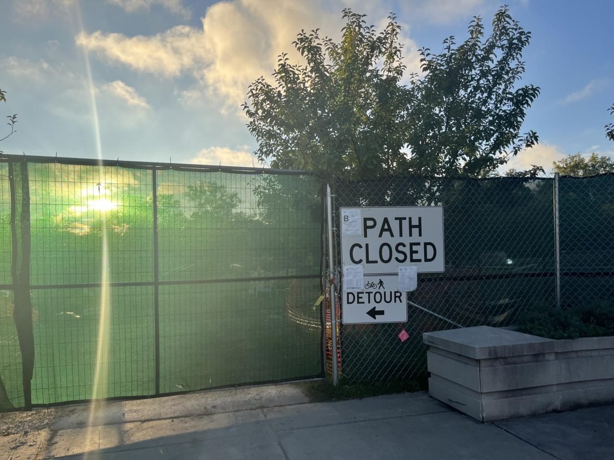 A construction site with a green fence and a sign that says “Path Closed.”