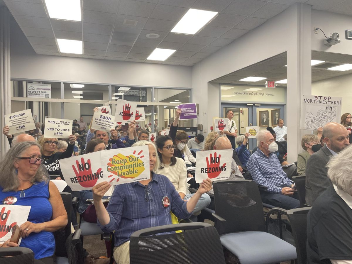 Audience members hold up anti-Ryan Field signs at the Land Use Commission meeting Wednesday night. Public commenters and community organizations voiced their thoughts on NU’s plan to rebuild Ryan Field and host for-profit concerts there, but the meeting will continue on Oct. 11. 