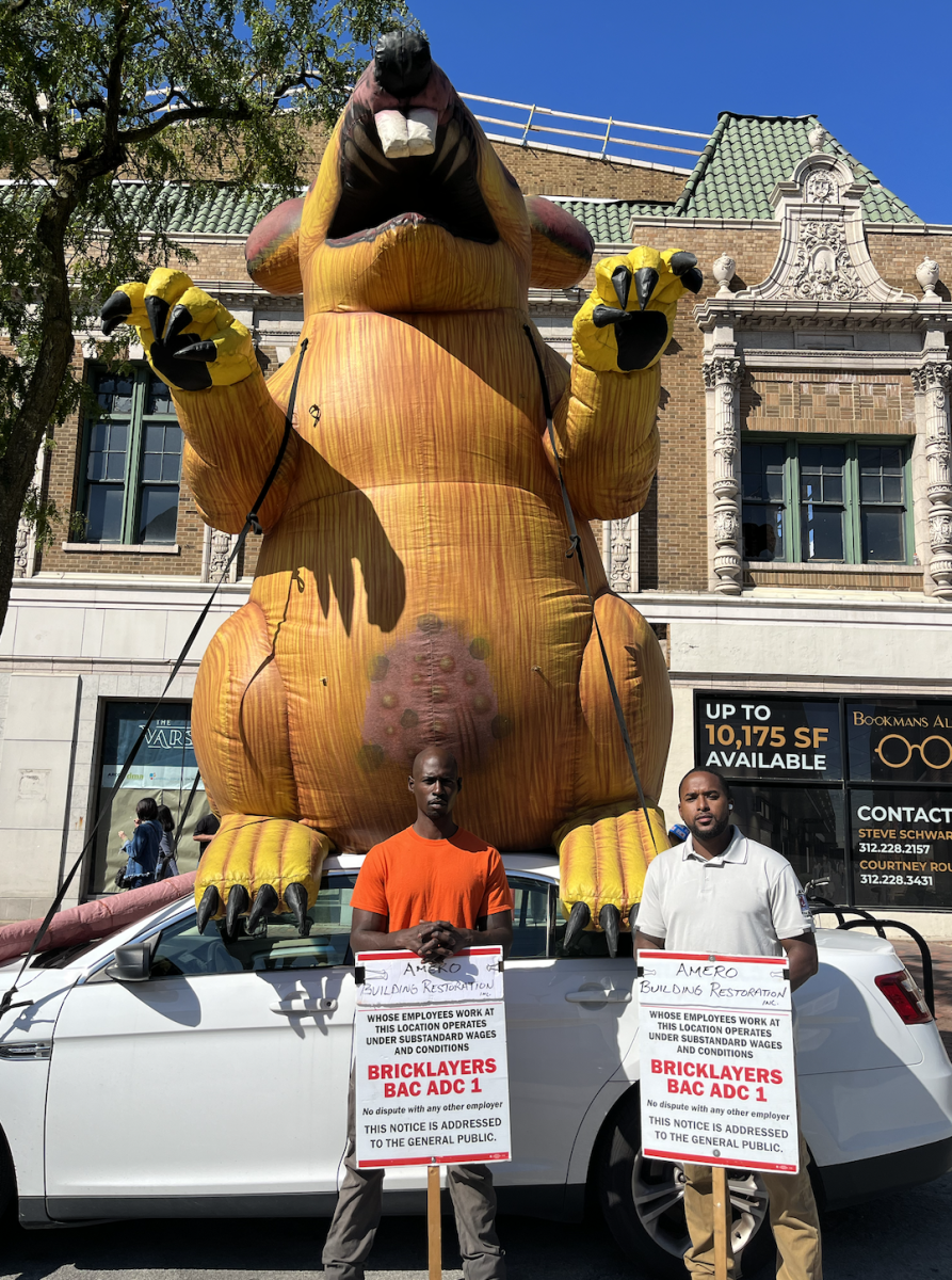 Members of the International Union of Bricklayers and Allied Craftworkers stand in front of the inflatable rat on Sherman Avenue.