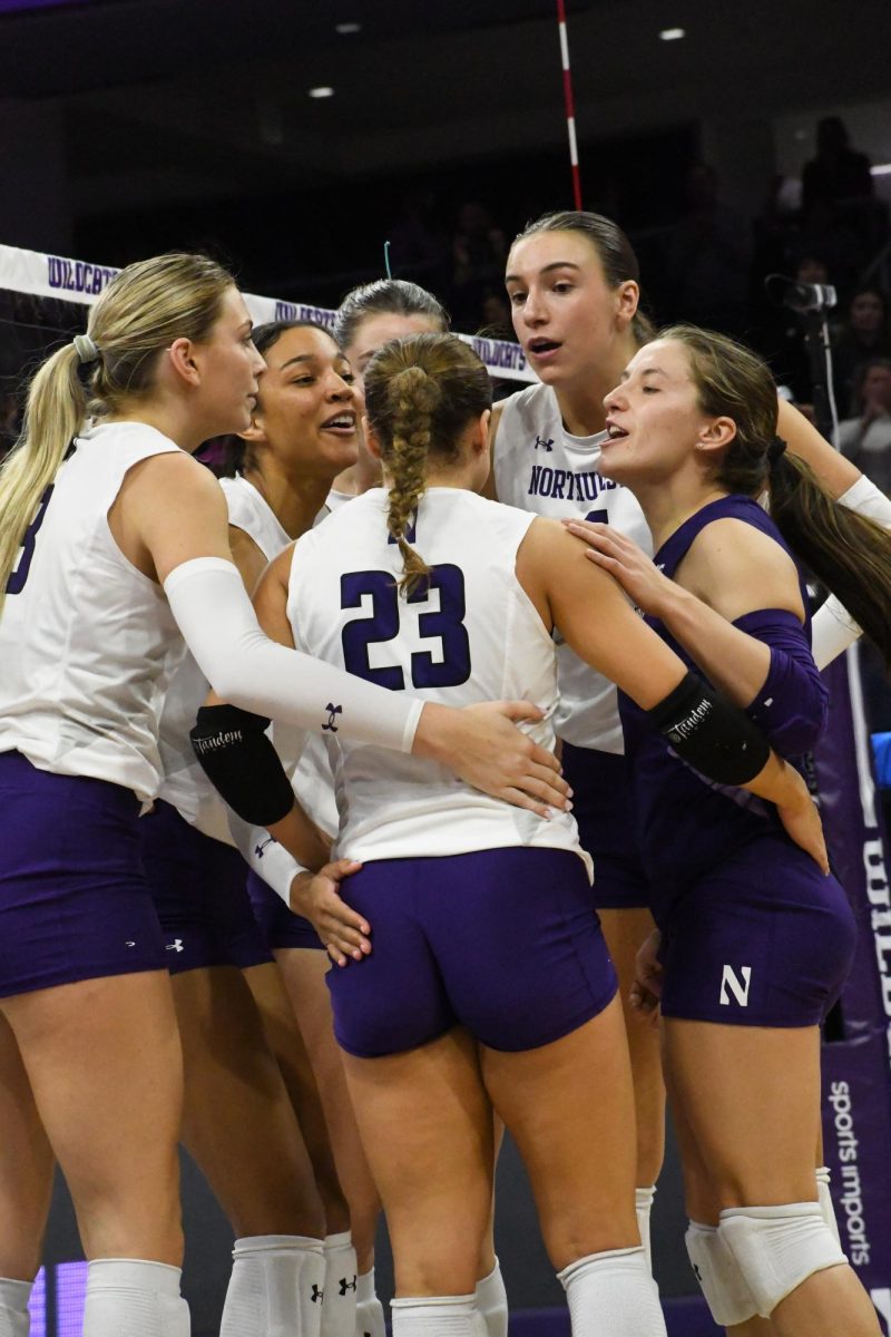 A group of players in purple and white uniforms stand in a huddle.