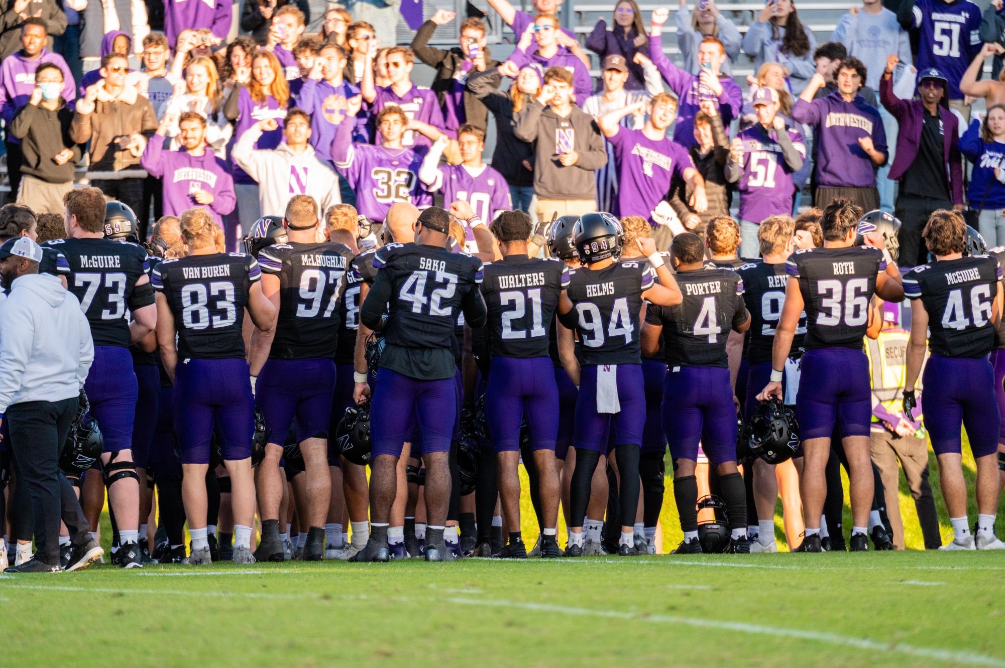 A group of football players stand in front of a crowd. 