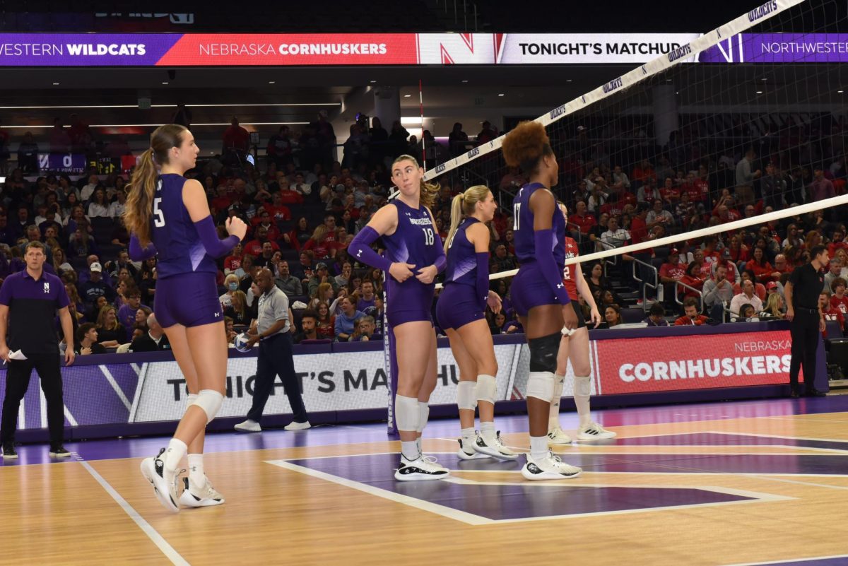 Players in purple and white jerseys stand at a volleyball net.