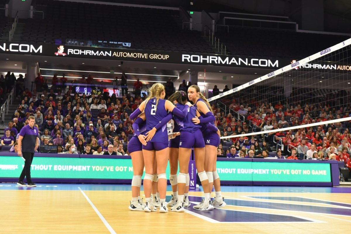 Players in purple and white jerseys form a huddle on the court. 