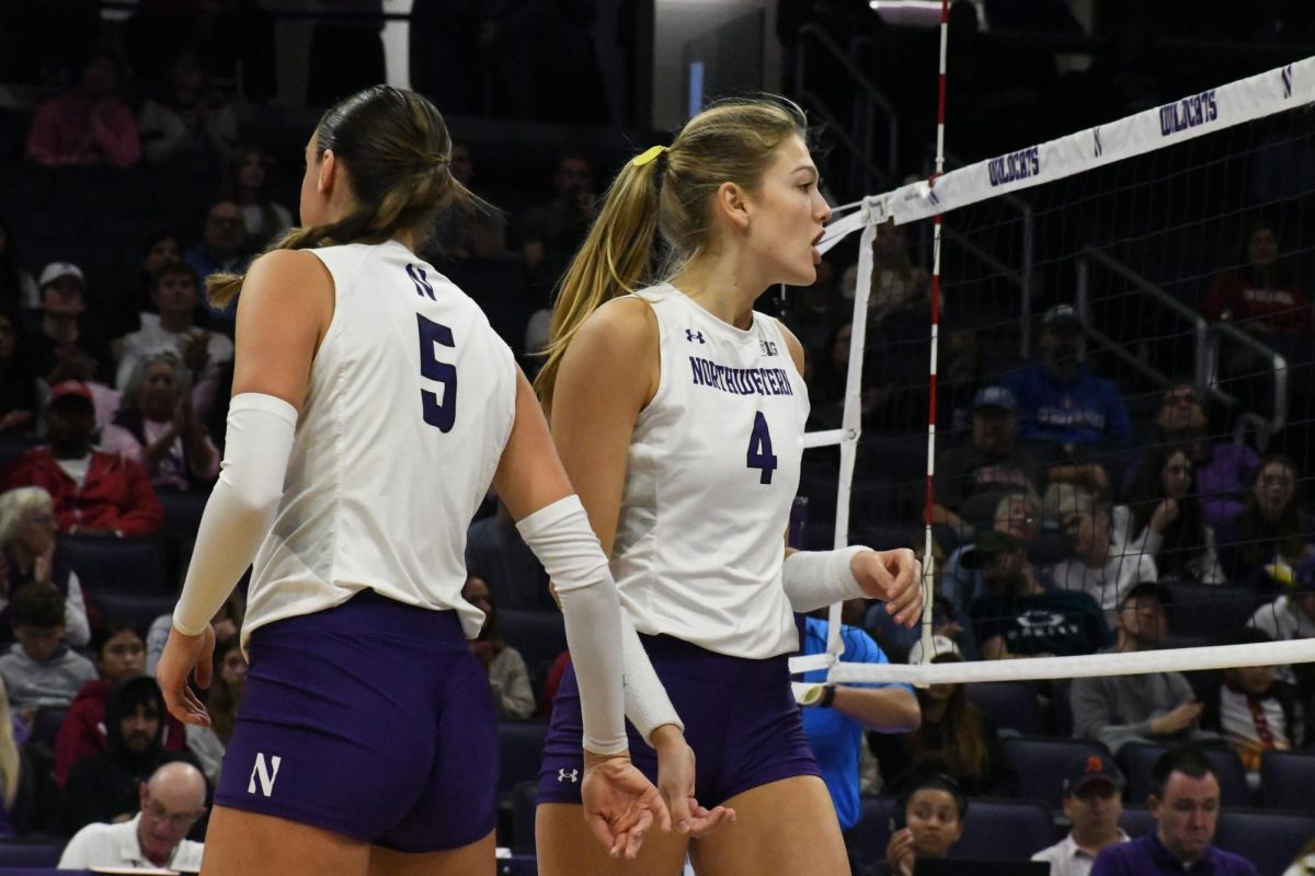 Two players in white and purple volleyball uniforms walk past one another.