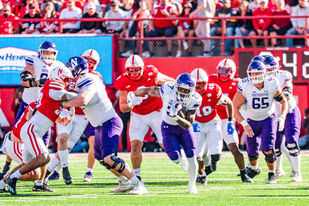 A player in purple and white fights a player in red and white as they run with the football.