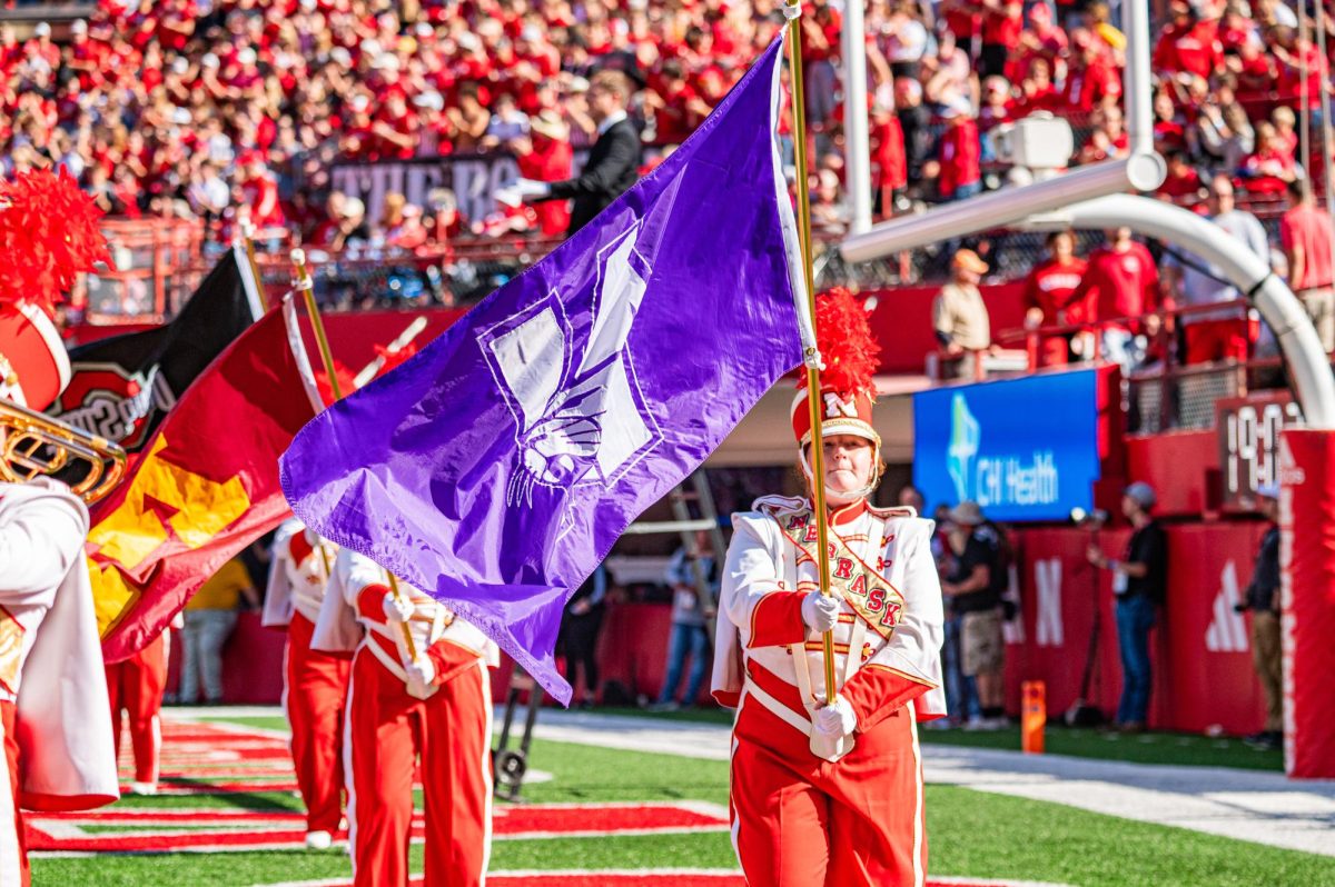 A marching band student in red and white hoists a purple Northwestern flag on a football field.