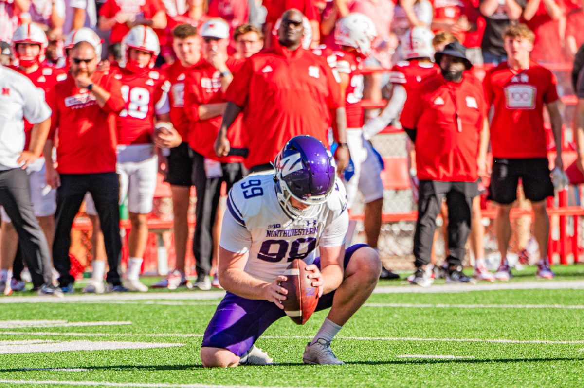 A player in purple and white sets a football down on the field.