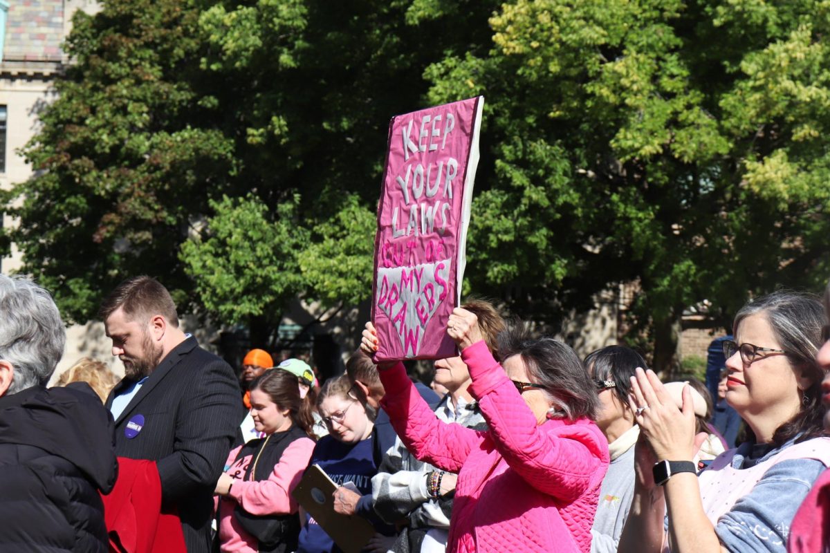 A person wearing pink stands in the middle of a group of people holding a sign up with two hands.
