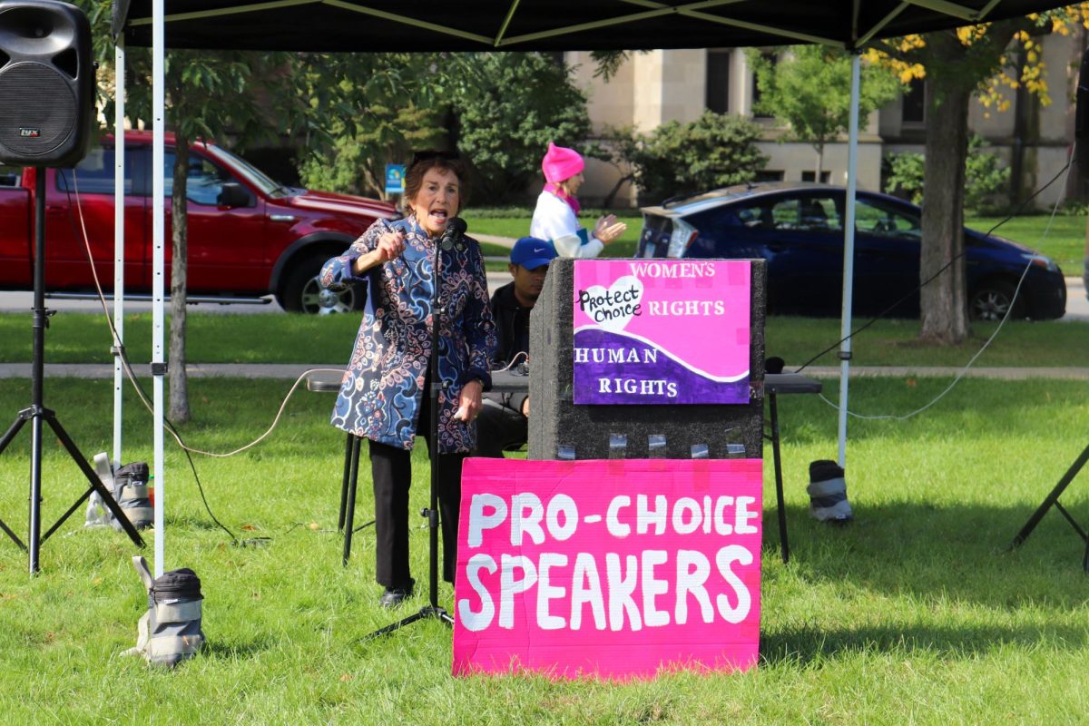 A person speaks into a microphone next to a pink sign.