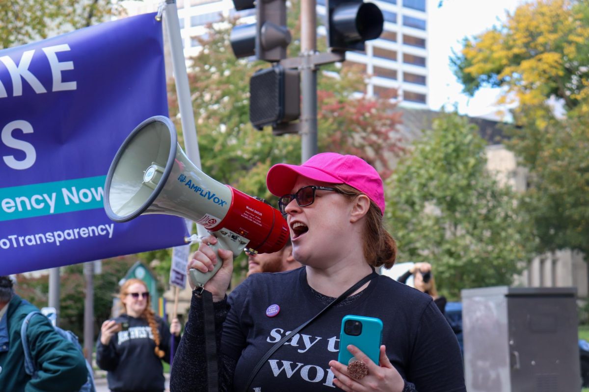 A person wearing a pink baseball cap speaks into a megaphone.
