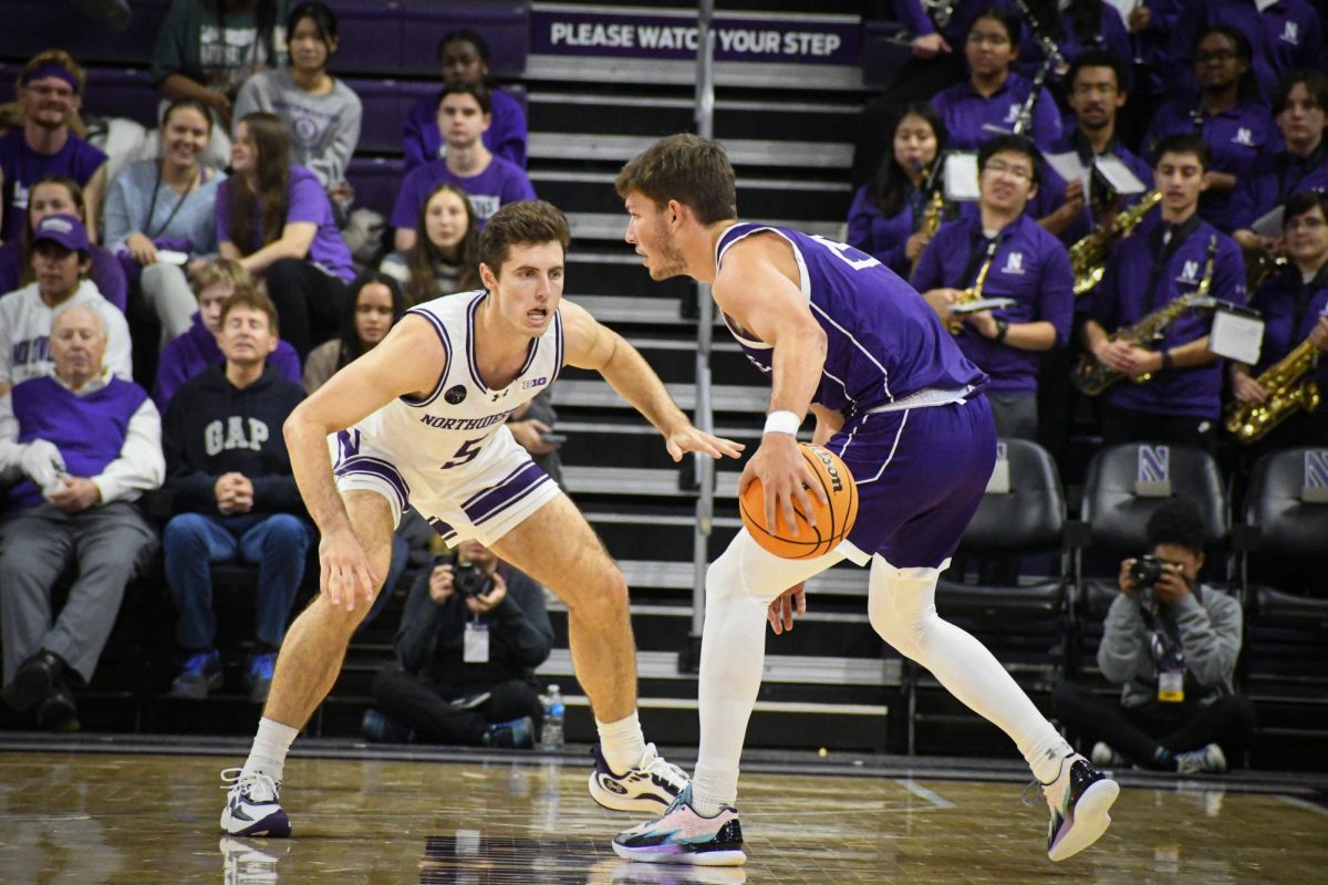 A player in a white and purple basketball uniform guards a player in a purple jersey.