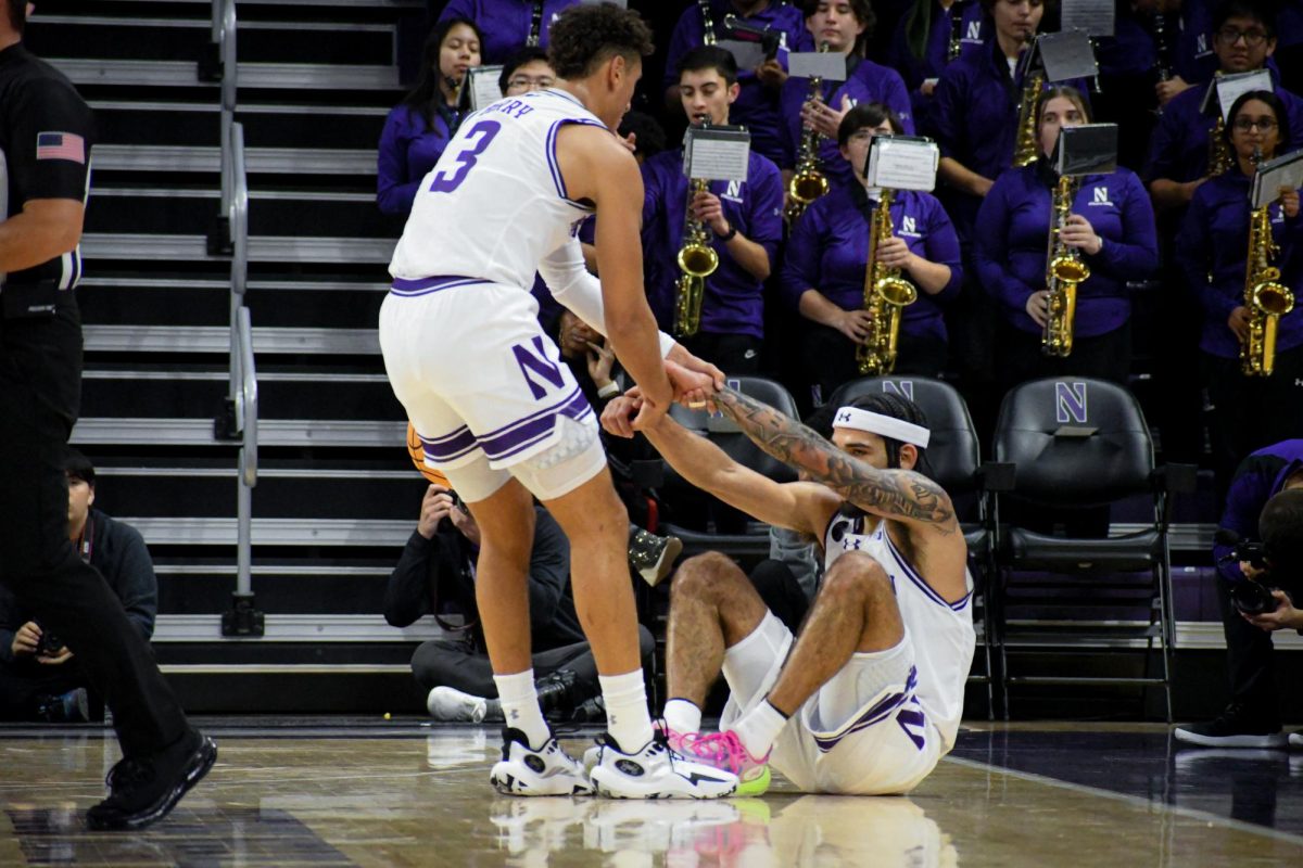 A player in a white and purple basketball uniform helps another player off the ground. 