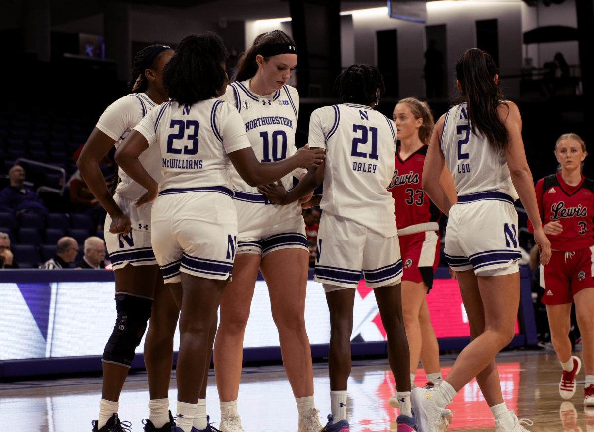 A group of basketball players wearing purple and white break a huddle with players wearing red walking in the background.