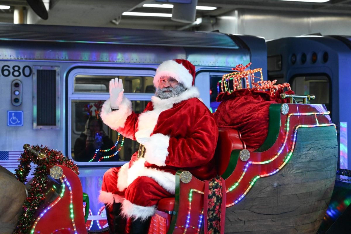 A person wearing a Santa outfit waves from a flatbed railcar.