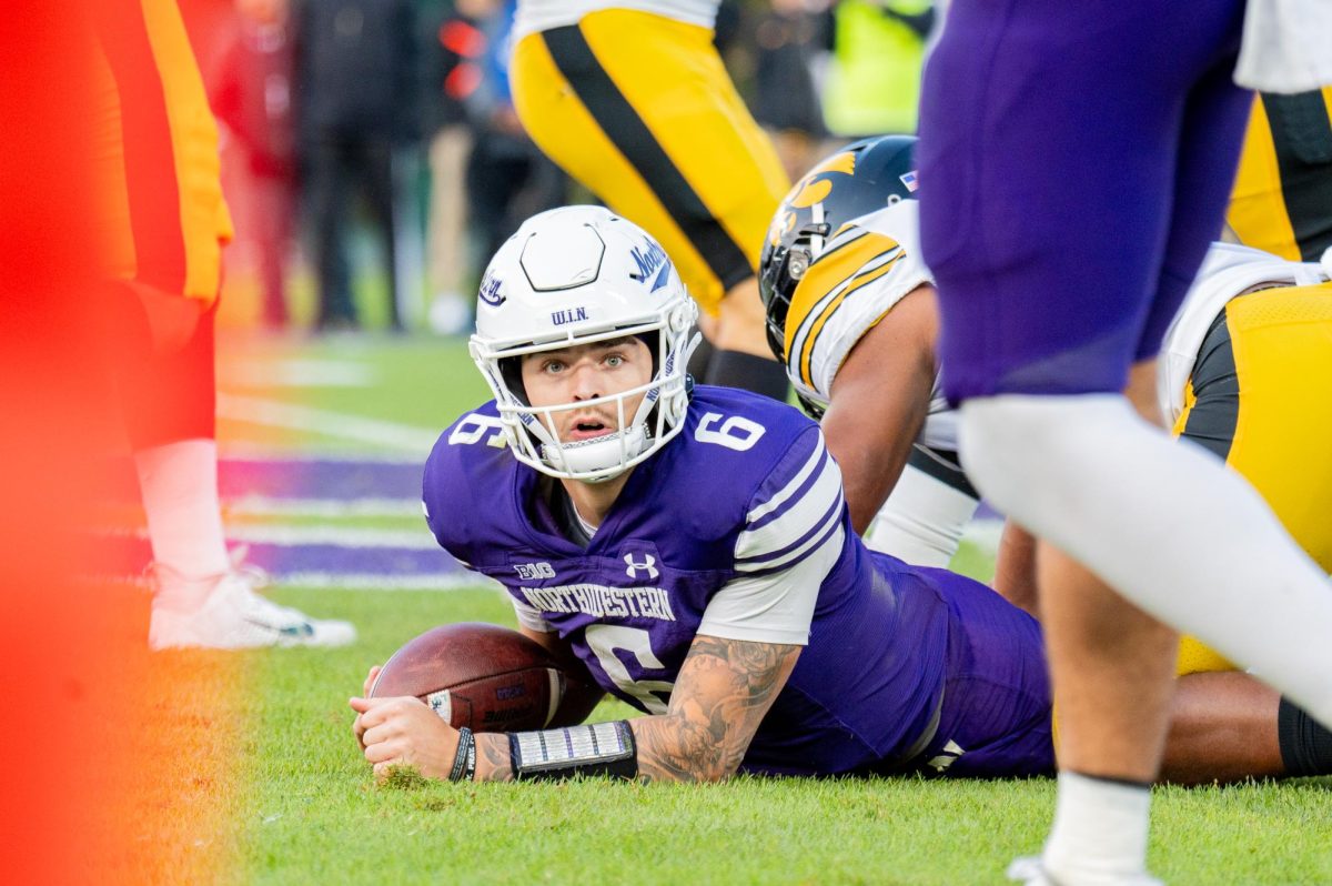 A player in purple and white looks up from the ground while holding a football.