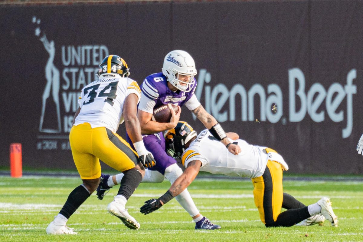 A player in purple and white makes their way through the opposing team’s defense while holding a football.