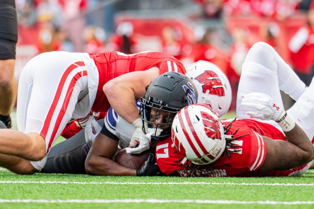 A football player holding a ball is tackled to the ground.