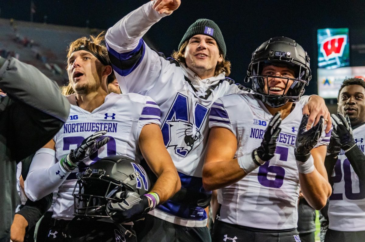Three football players in purple and white cheer after winning the game.
