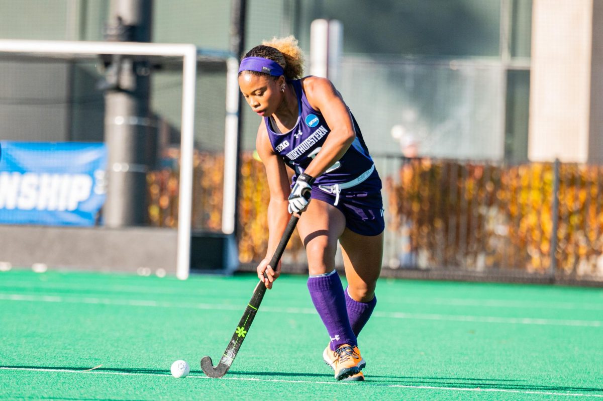 A field hockey player in purple gets ready to hit the ball.
