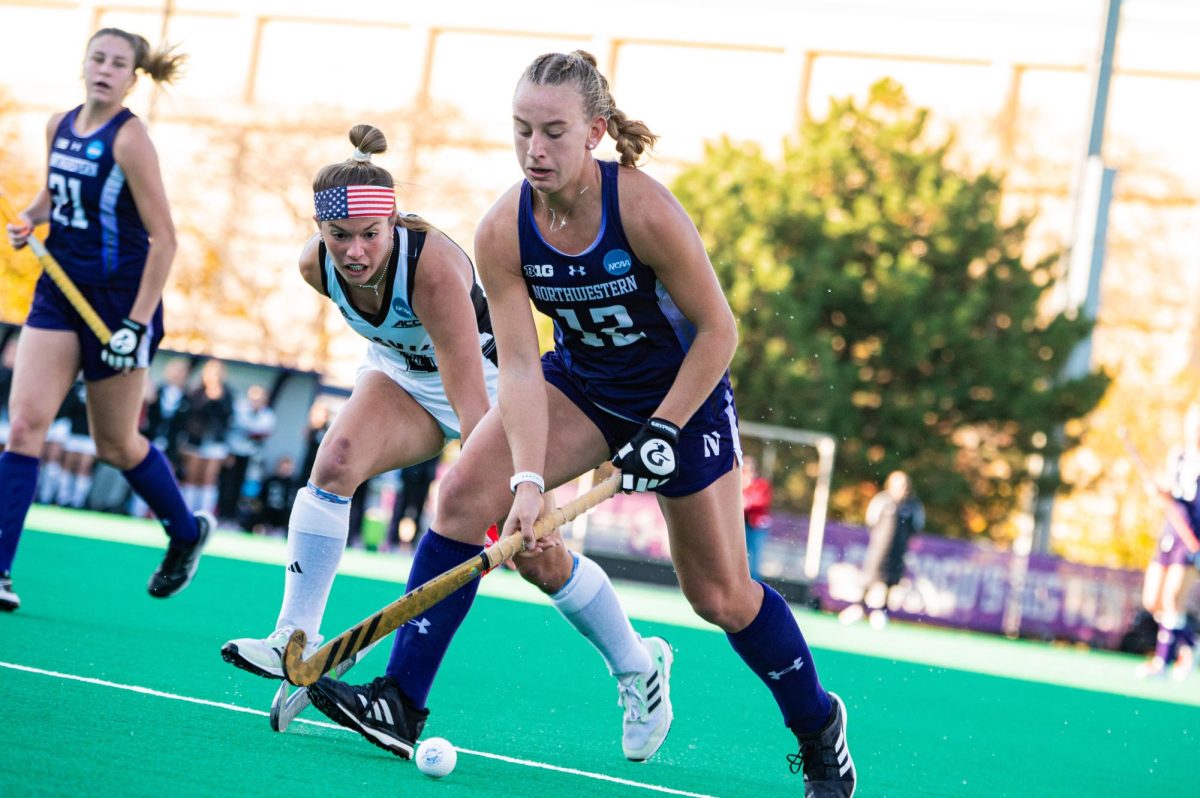 A field hockey player in purple hits the ball.