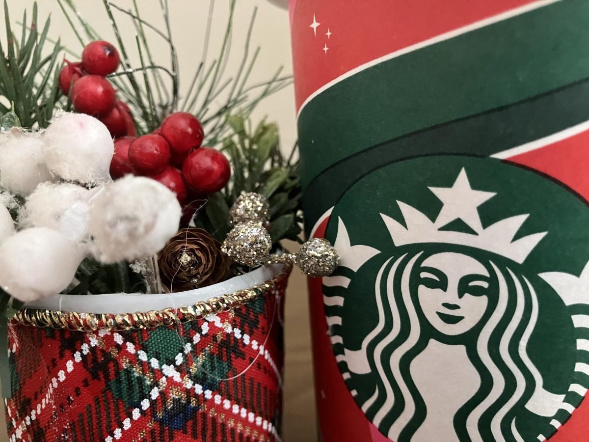 A small red and green basket containing silver, red and white balls, and a pinecone sits next to a red and green cup featuring the Starbucks logo.