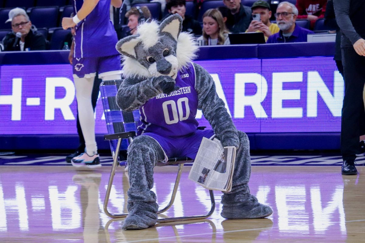 A Wildcat mascot wears a purple basketball uniform and sits on a lawn chair while holding a copy of The Daily Northwestern.