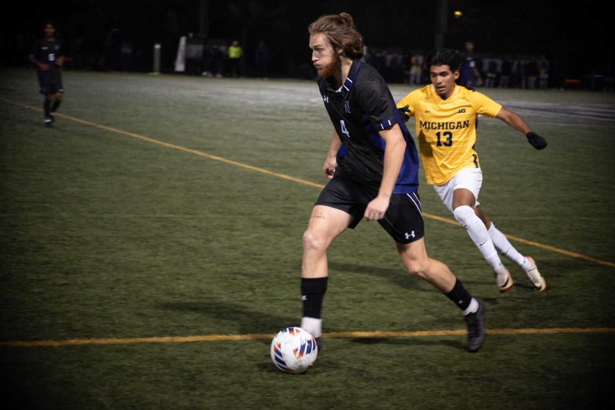 A player in a black jersey dribbles the ball away from a player in a yellow jersey.