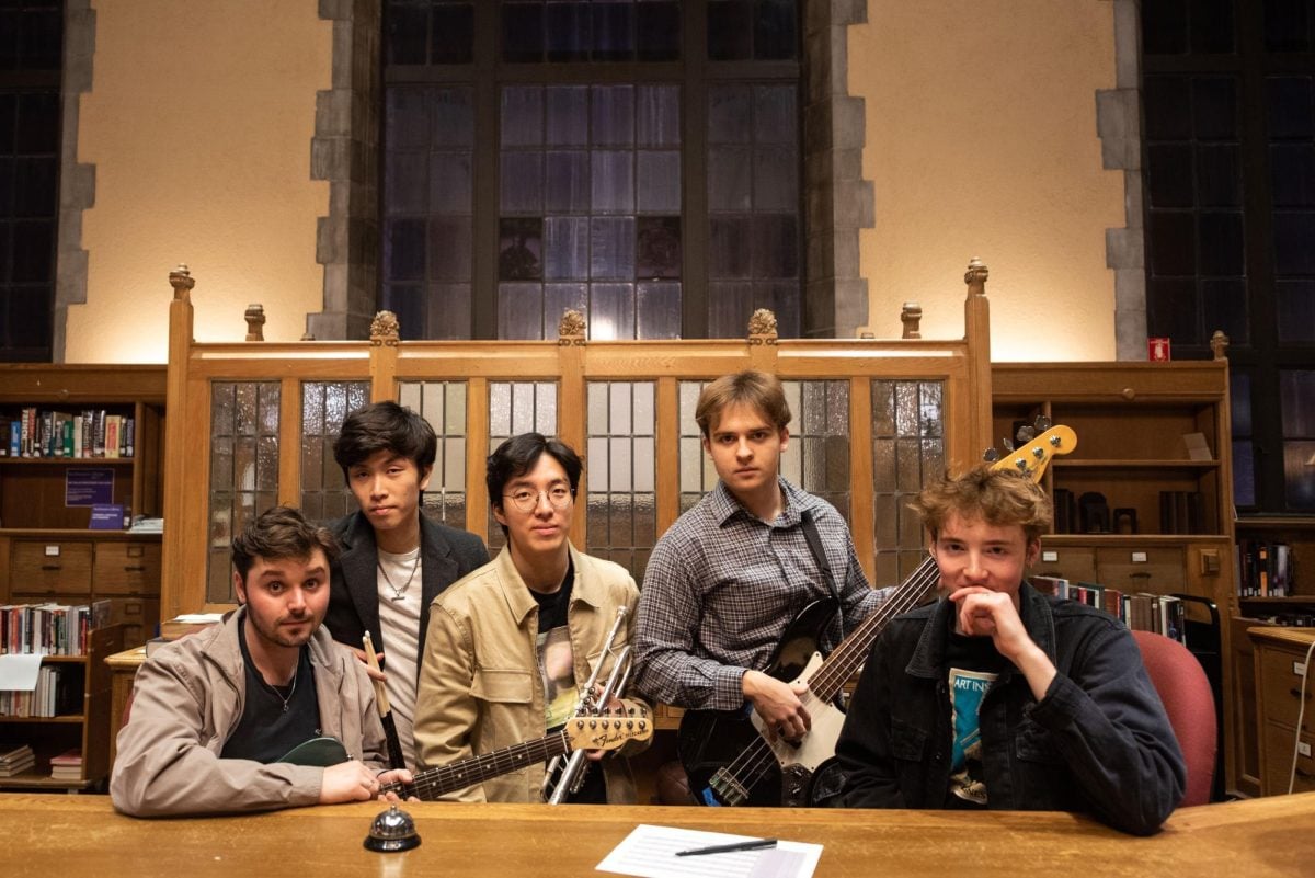 Five musicians stand behind a library desk, holding their instruments.