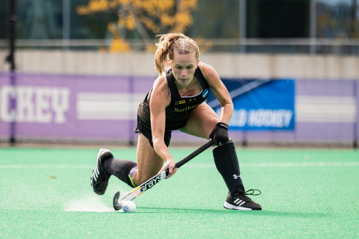 A field hockey player in black hits the ball.