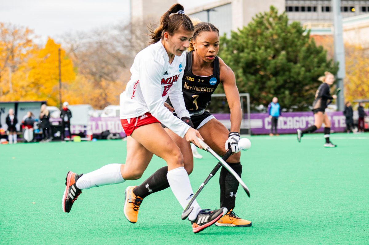 Two field hockey players chase after the ball.