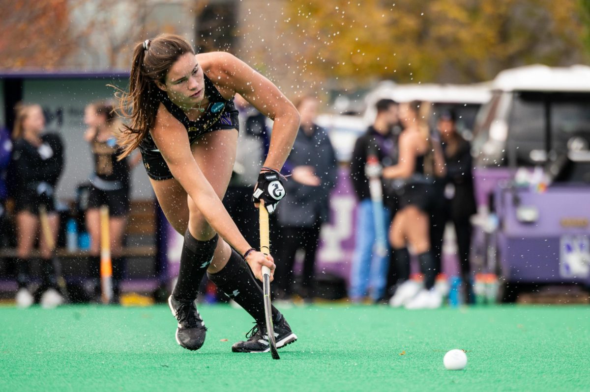 A field hockey player in black hits the ball.