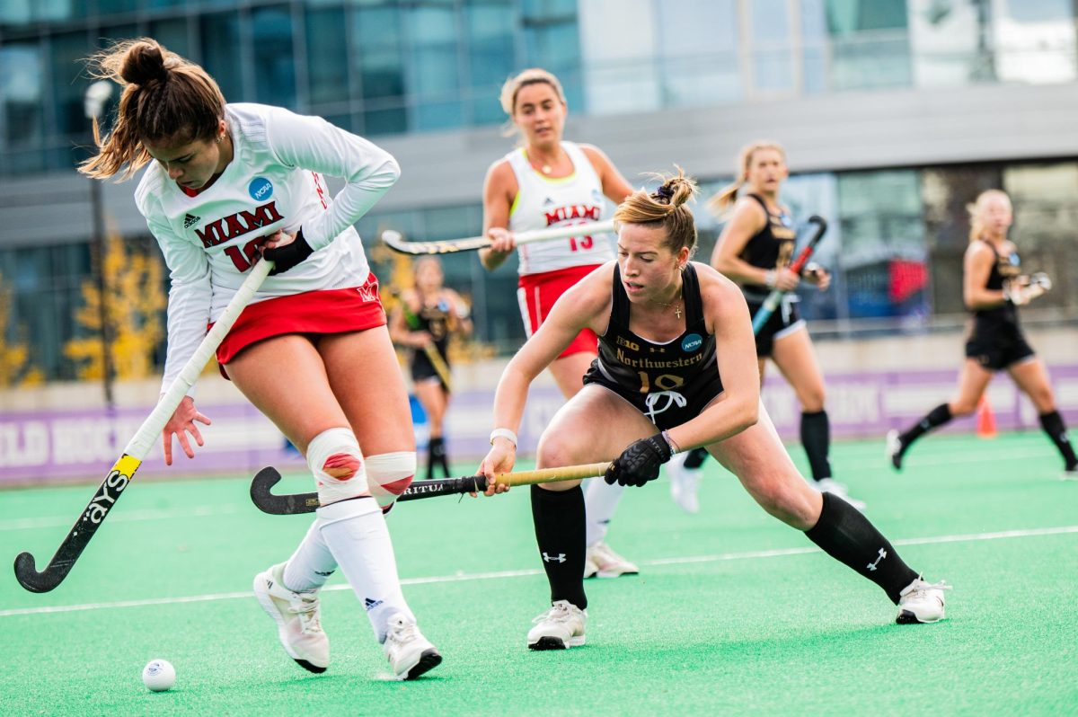Two field hockey players go after a ball.
