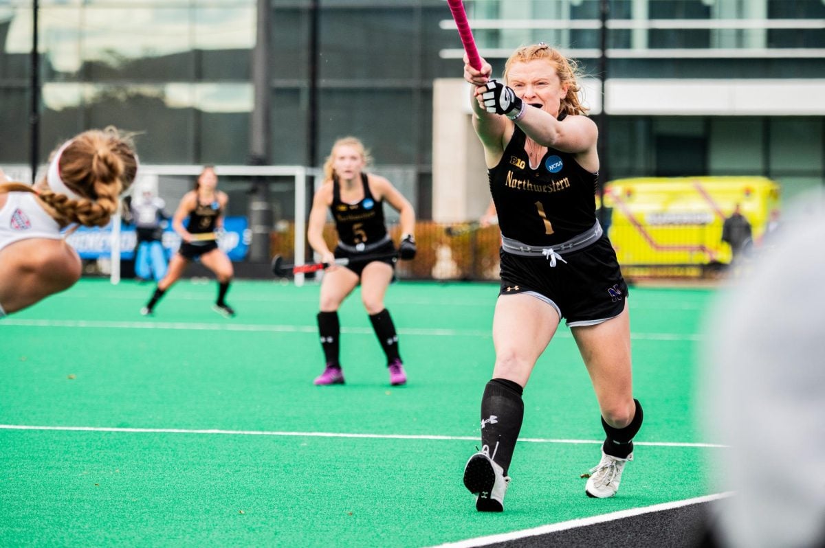 A field hockey player in black lifts the ball.