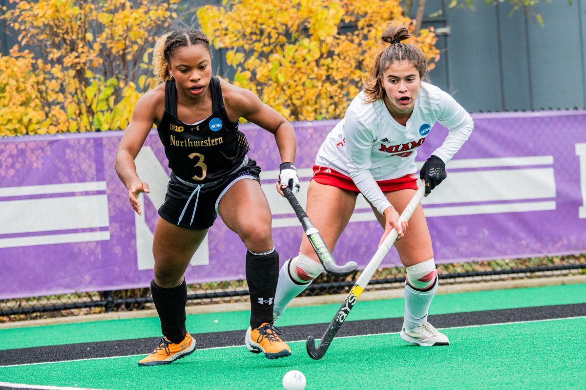 Two field hockey players go after a ball.