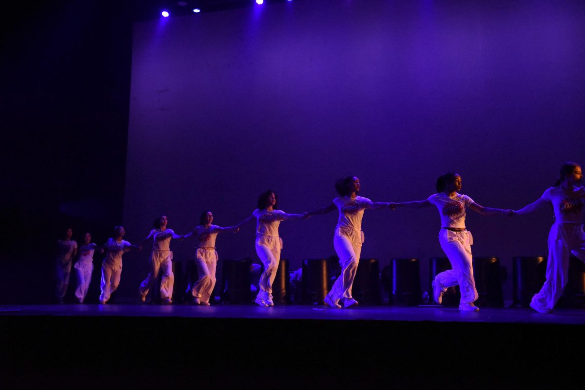 A group of dancers wearing white link hands.