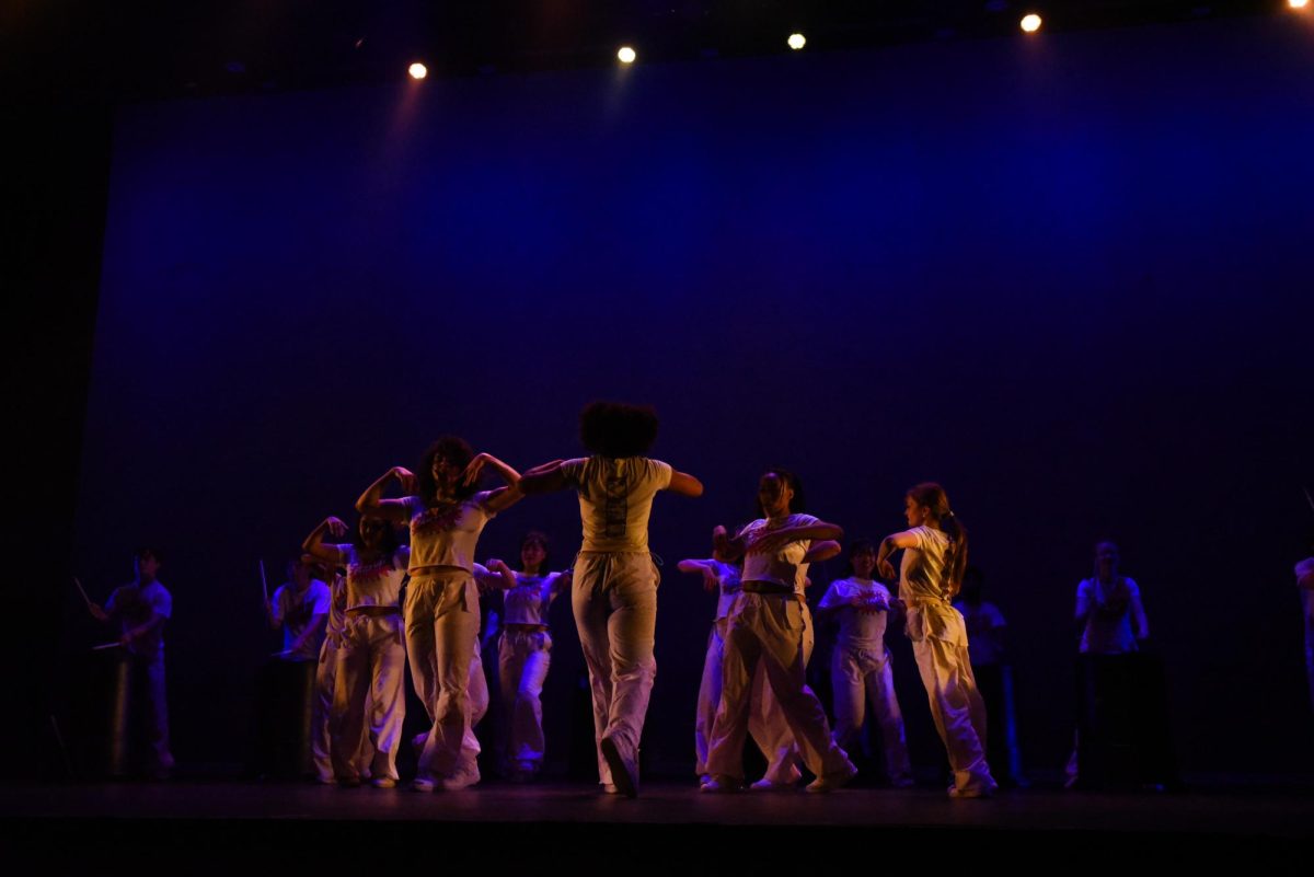 A group of dancers in white stand with their backs to the audience.