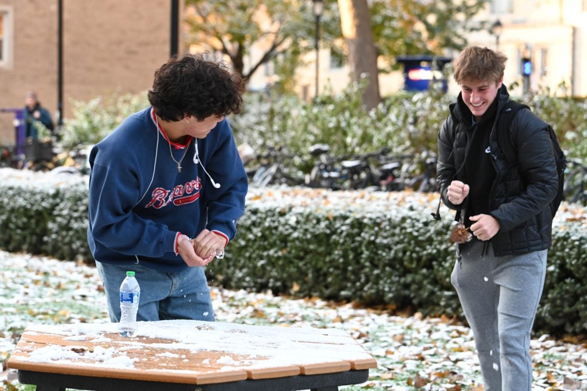A man wearing a blue sweatshirt and a man wearing a black jacket play with snow.