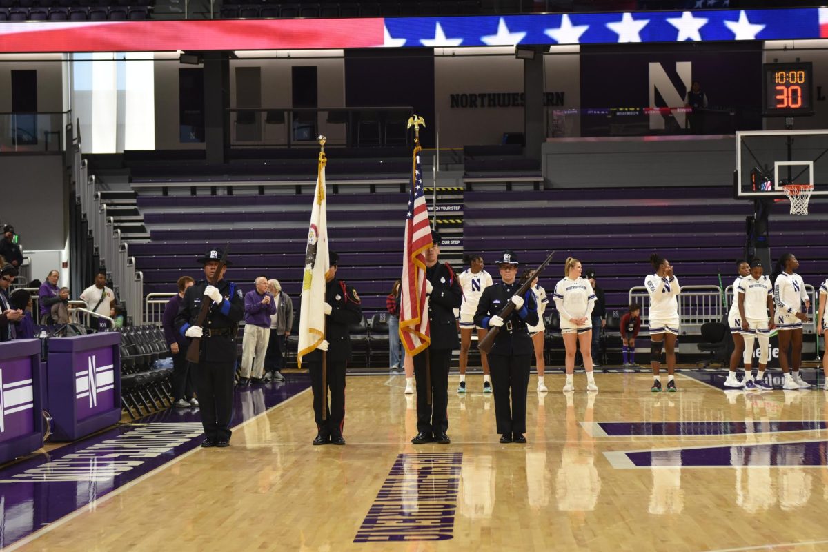 People in uniform hold rifles and an American flag on a basketball court. 
