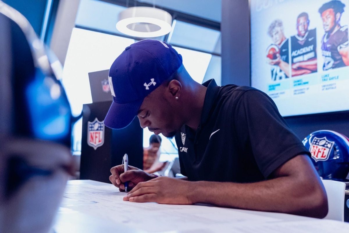 Defensive back Timi Oke signs his national letter of intent at an NFL Academy event in December 2023. Oke was one of 15 Wildcat commits to join David Braun’s inaugural recruiting class on National Signing Day.