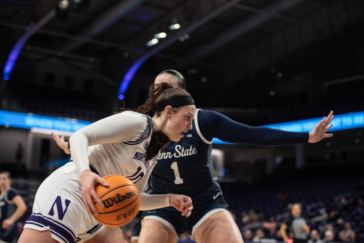 Junior forward Caileigh Walsh in a white jersey holds the ball and moves around Penn State’s Ali Brigham, a defensive player in a blue jersey.
