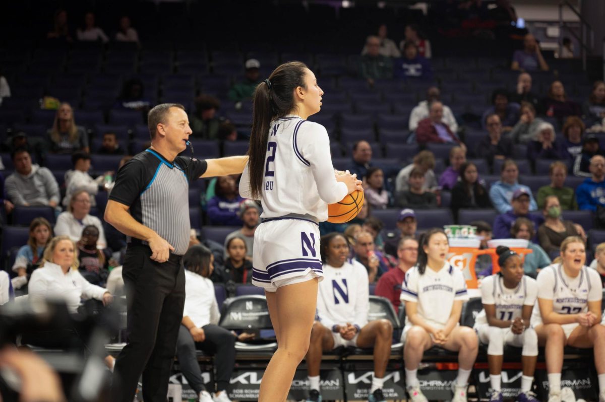 Basketball player Caroline Lau, who is wearing a white uniform, waits to pass the ball while a referee blows a whistle and points.