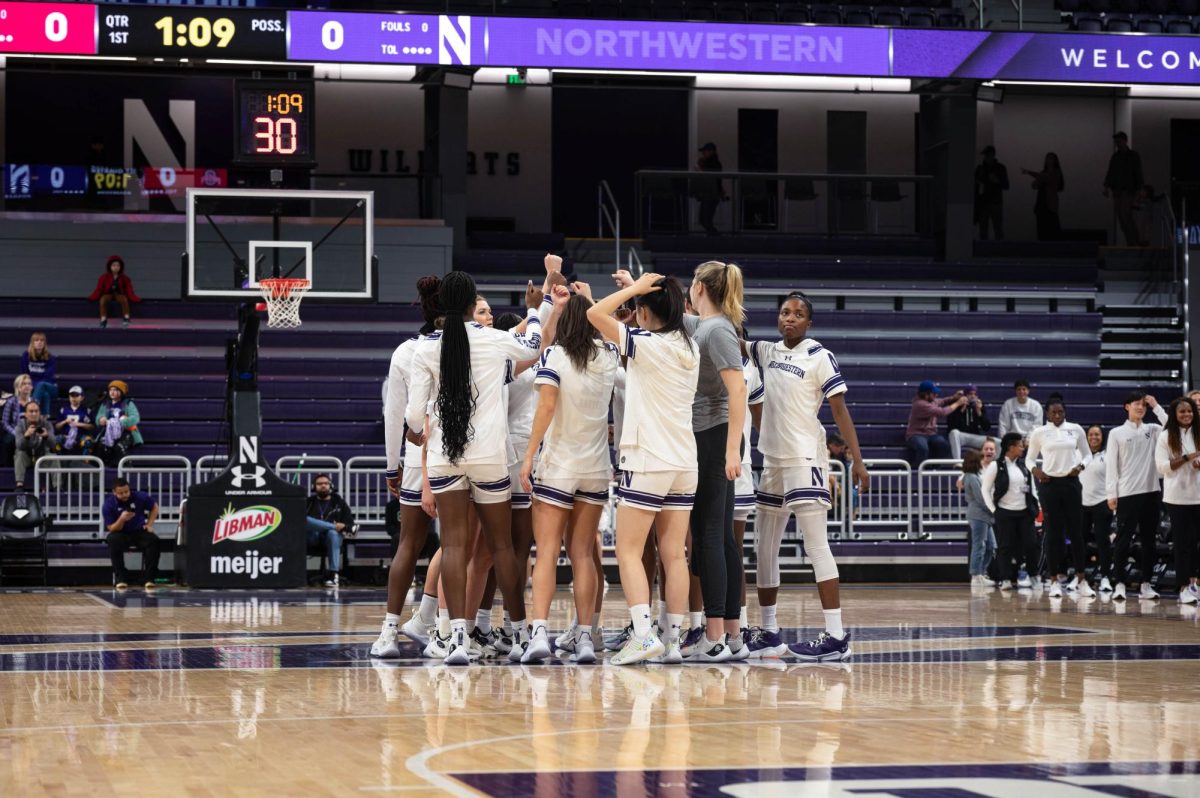 A group of basketball players wearing white uniforms stand in a huddle in the middle of the court.