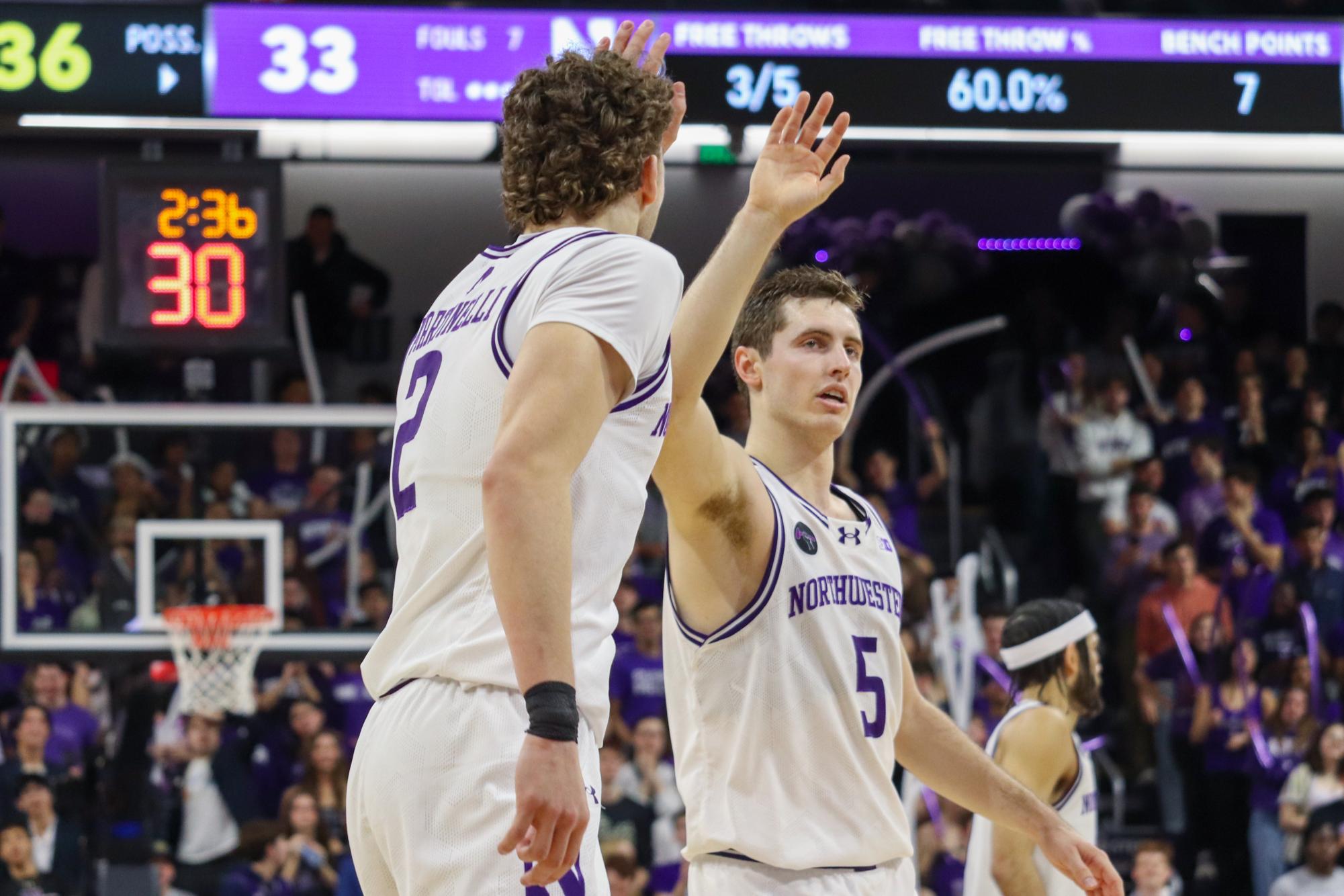 Northwestern’s graduate student guard Ryan Langborg and sophomore forward Nick Martinelli, both in white basketball uniforms, high-five each other in the middle of the court.